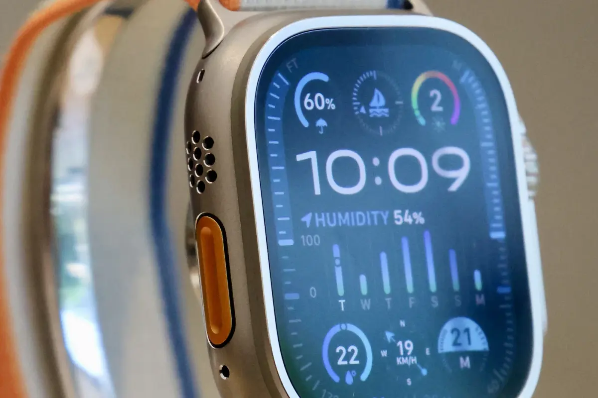 Gros plan sur une Apple Watch Ultra 2 en titane, bouton Action orange sur la tranche, cadran affichant l'humidité, la vitesse du vent et un indicateur de navigation