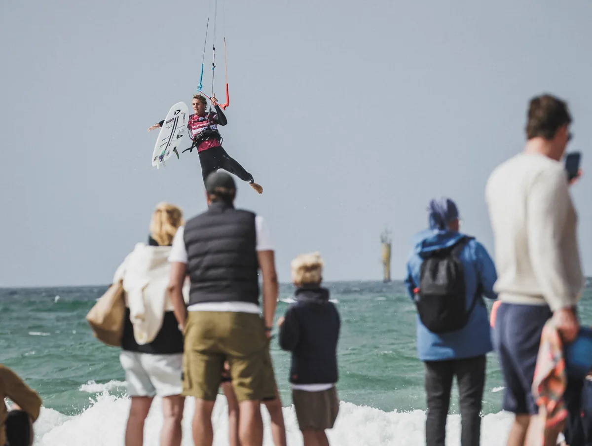 Spectateurs align&eacute;s sur le sable devant la mer, regardant un kitesurfeur en vol au-dessus de l'eau