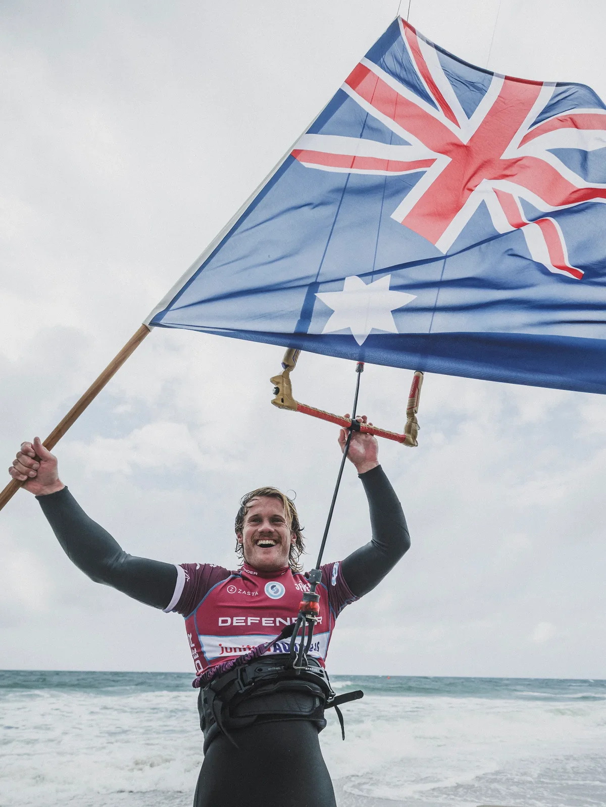 James Carew, en lycra de comp&eacute;tition bordeaux, brandissant un grand drapeau australien devant la mer