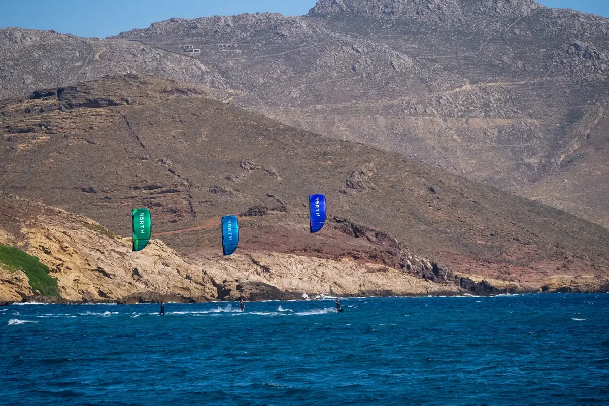 Trois kitesurfeurs naviguent de front sous des ailes North verte, bleu clair et bleu fonc&eacute;, devant une c&ocirc;te rocheuse
