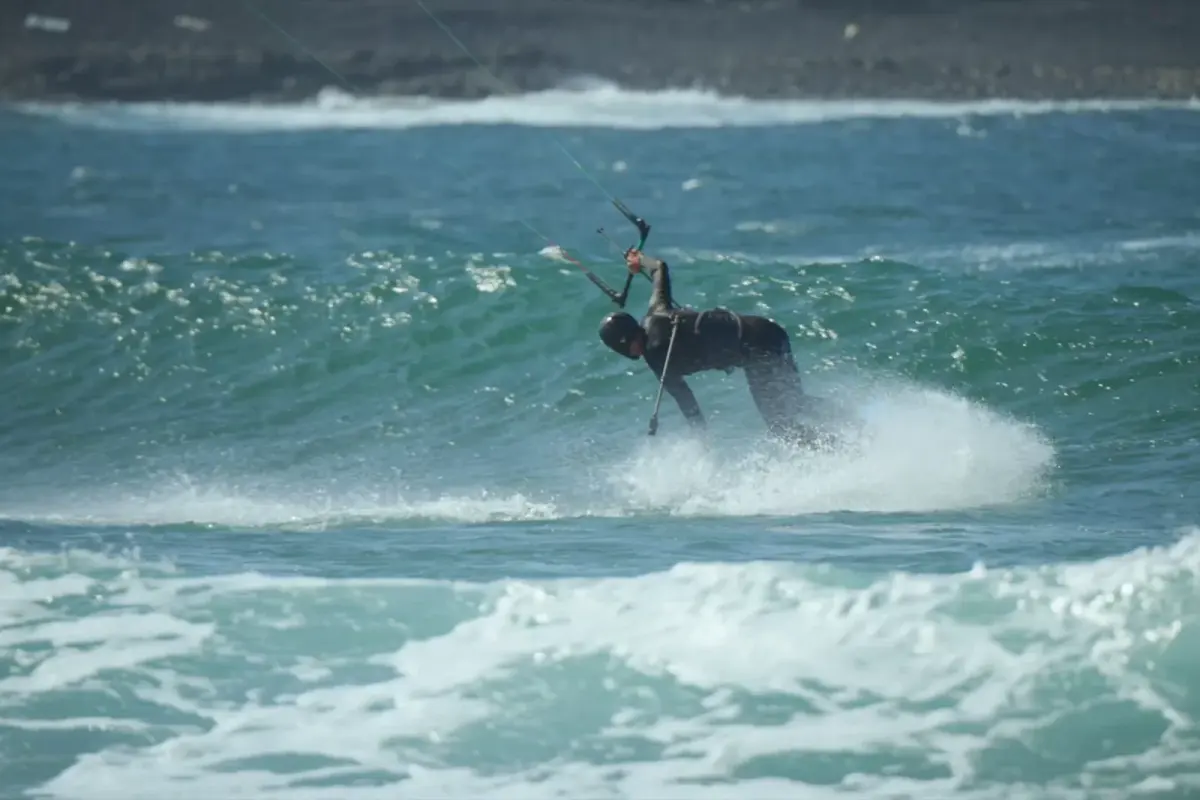 Un kitesurfeur engage un virage dans les vagues sous son aile, cadré au ras de l'eau comme depuis un mât caméra posé sur l'eau
