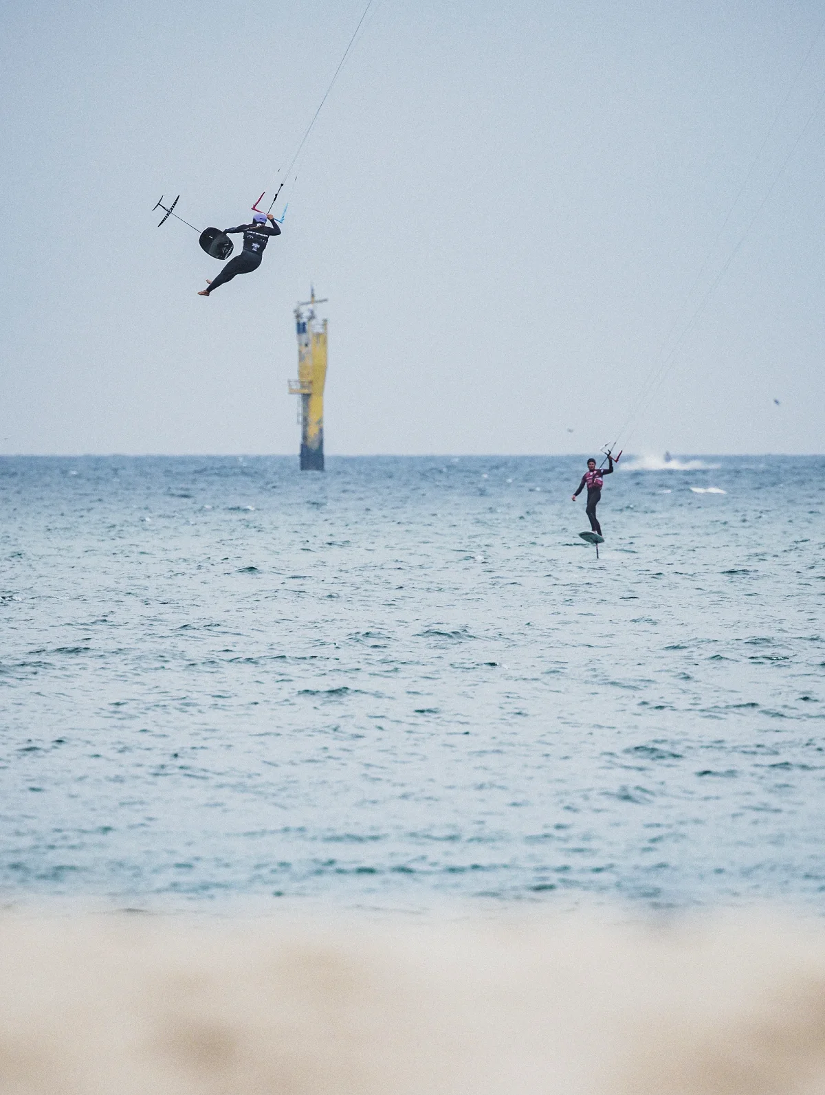 Une rideuse d'hydrofoil tr&egrave;s haut au-dessus de la mer, planche &agrave; foil aux pieds, une seconde rideuse en vol rasant au loin