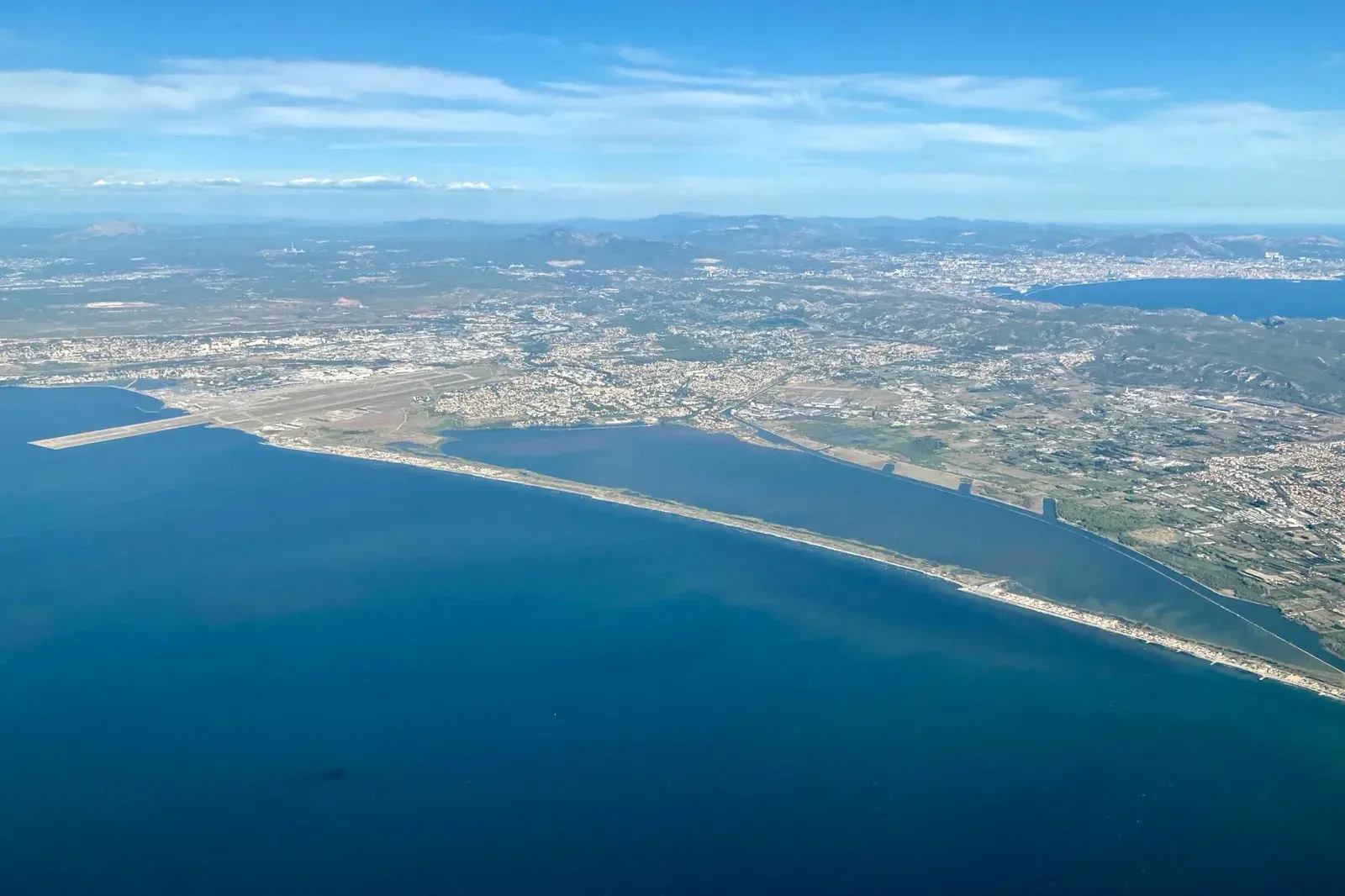 Vue aérienne du cordon du Jaï séparant l'étang de Berre de l'étang de Bolmon, la piste de l'aéroport de Marignane à gauche et Marseille au fond