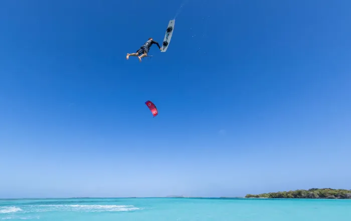 Kitesurfeur en plein board-off très haut au-dessus d'un lagon turquoise, planche Duotone grise tenue à la main et aile rouge loin en dessous de lui
