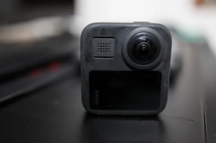 Gros plan de face sur une caméra 360 GoPro posée sur une table sombre, objectif hémisphérique bombé au centre du boîtier