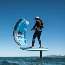 Rider en foil au-dessus de l'eau, tractant une parawing bleue sans boudin ni latte, les lignes tendues vers une barre courte tenue à deux mains
