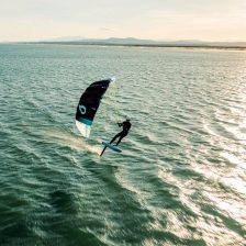 Rider en foil tractant une petite aile souple sans latte au-dessus de l'eau, lignes fines tendues vers une barre courte