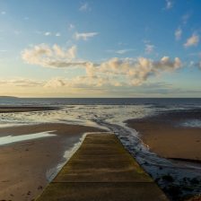 Plage à marée basse en fin de journée, mer repoussée très loin, cale de mise à l'eau et bancs de sable humide sous une lumière rasante