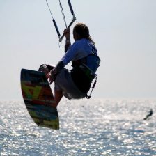 Kitesurfeur en vol au-dessus d'une mer scintillante, sa planche twintip saisie à la main, barre tenue à bout de bras